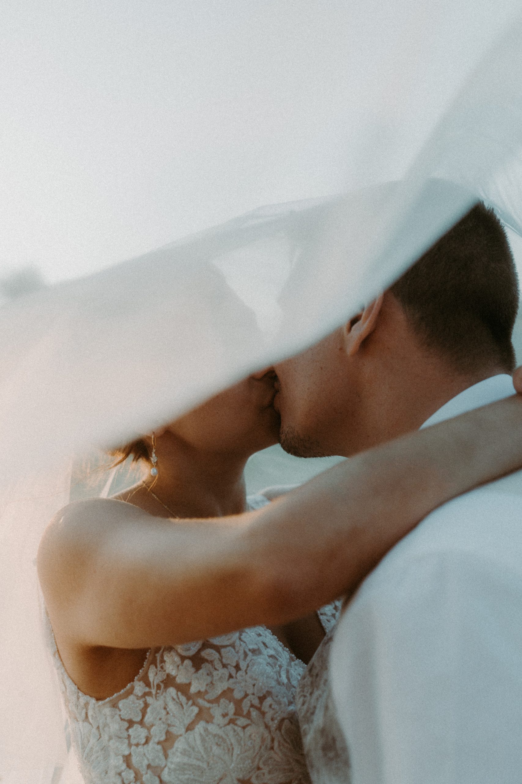 Un couple de mariés s'embrassent sous un voile au coucher de soleil au domaine du bijoutier